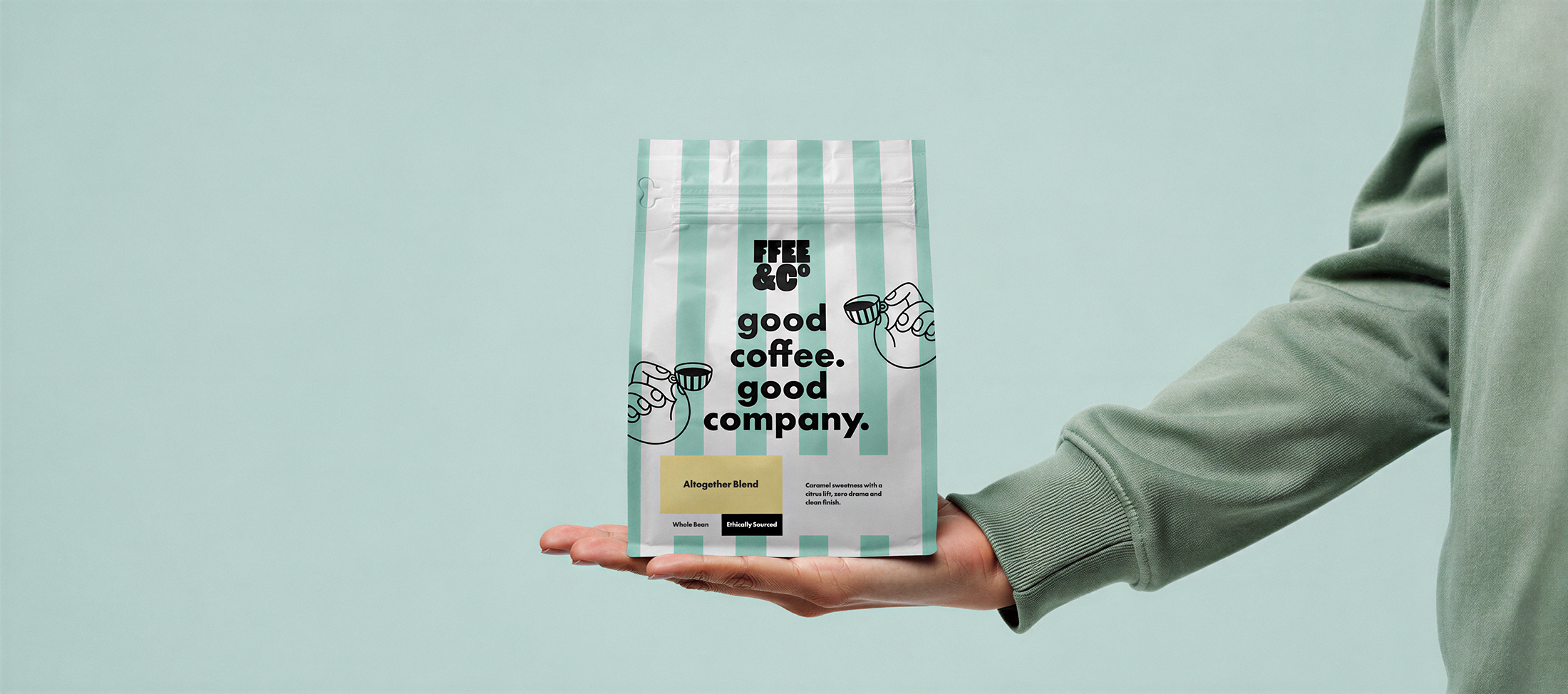 Person holding a bag of Ffee & Co 'good coffee. good company.' coffee on a light green background