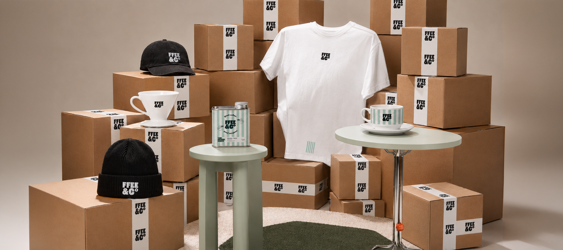 Stack of Fffee & Co brown boxes with white t-shirt, black hats, and other items on a beige background