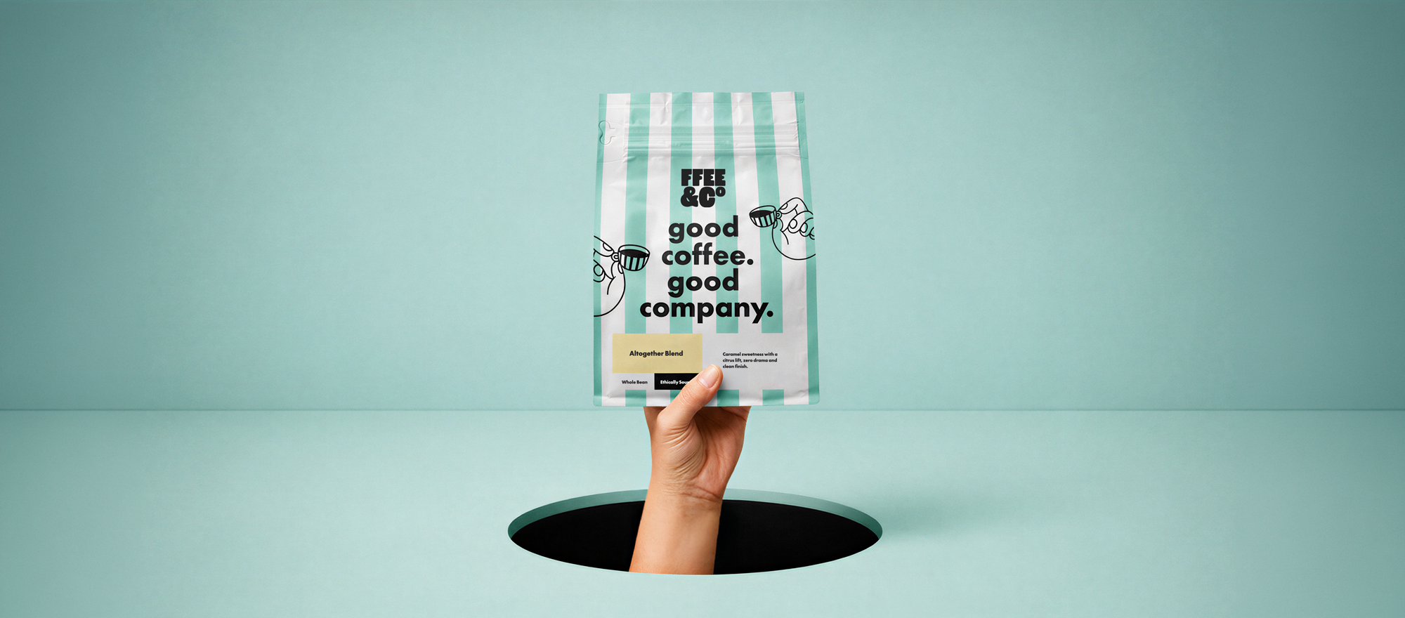 Hand holding a Ffee & Co coffee bag labeled 'Good Coffee, Good Company' above a hole in a light blue background